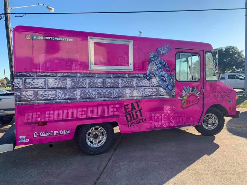 Pink truck with an astronaut on it parked nearby some cars